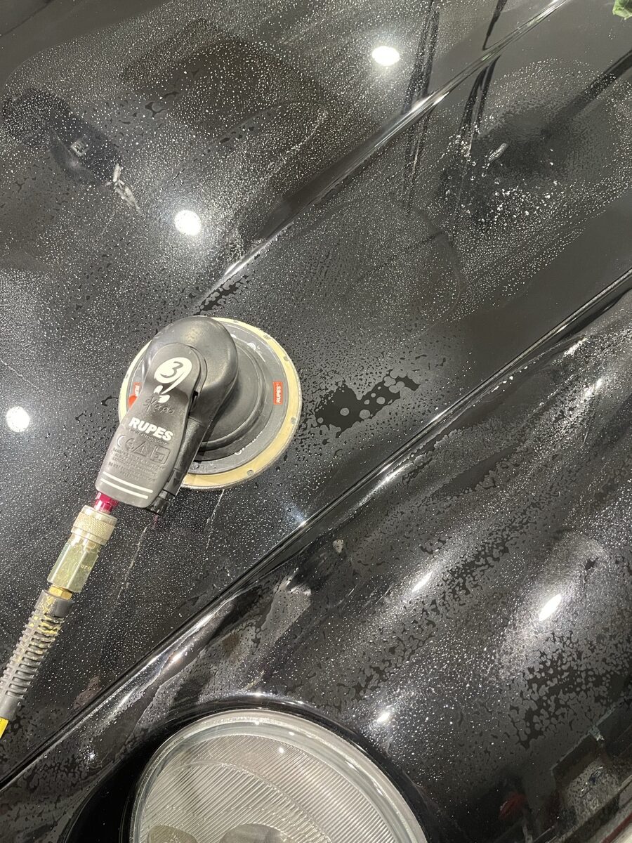 Close-up of Rupes polisher compounding black car paint near headlight removing swirl marks and oxidation at CBA Detailing Bergen County NJ